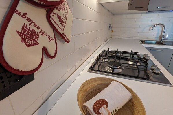 Cocina moderna con baldosas blancas, estufa a gas y un tazón de madera con una toalla.