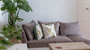 Ein Wohnzimmer mit grauem Sofa, zwei gemusterten Kissen, einem Holztisch und einer Topfpflanze.