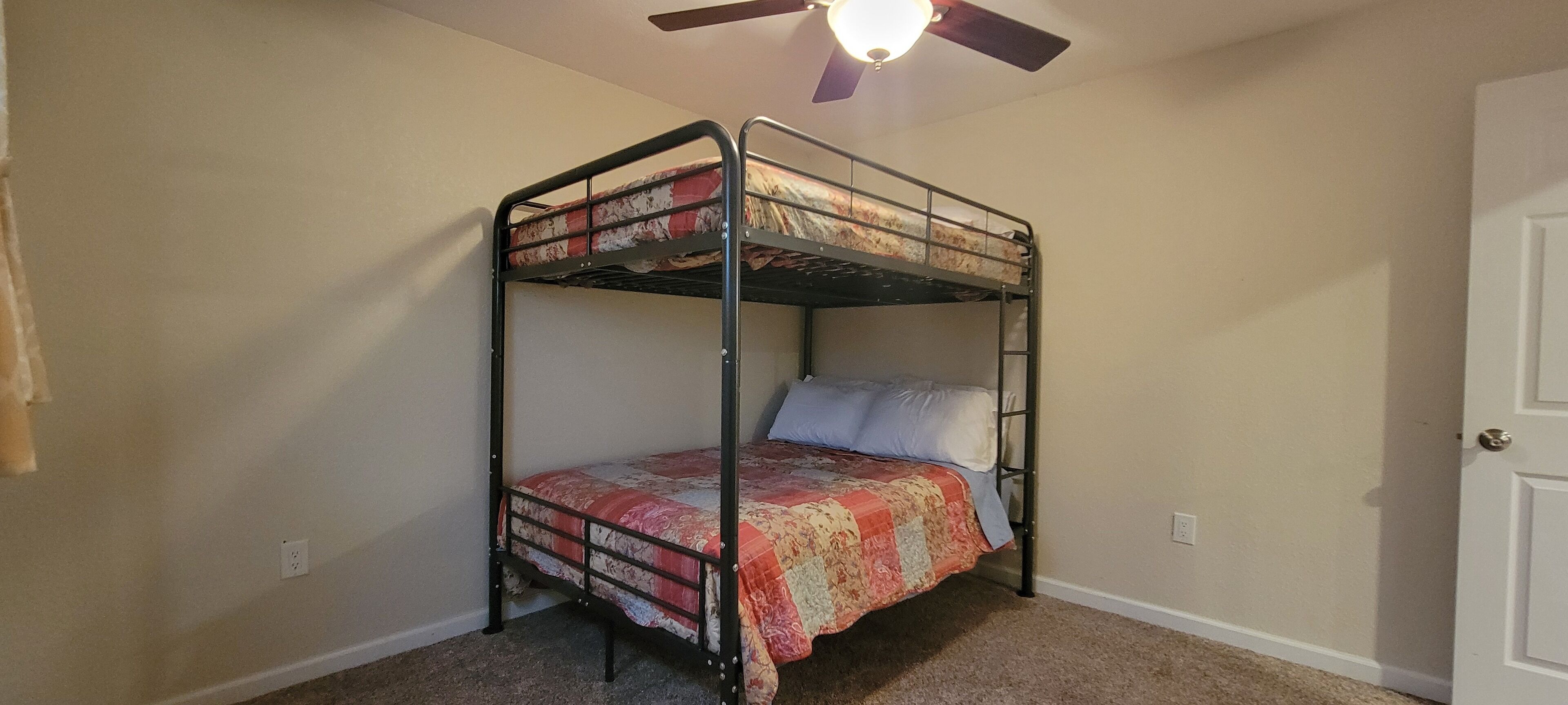 A bunk bed with a red and beige quilt, a ceiling fan, and a white door.