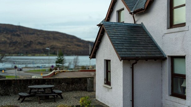 Une maison avec un toit en pente, un petit porche et une vue sur un lac et des montagnes.
