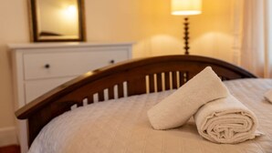Un lit bien fait, avec une serviette enroulée, une tête de lit en bois, une table de chevet avec une lampe et un tableau encadré accroché au mur.