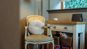 Une chaise avec un coussin, une petite table avec une tasse et un haut-parleur posé sur un bureau.