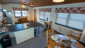Une cuisine compacte dotée d’un îlot central, d’un plafond en bois et d’un coin repas avec une table dressée pour deux personnes.
