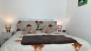 Een slaapkamer met een bed, voorzien van een plaid en kussens met een stierpatroon, een bedlampje en een schilderij aan de muur.