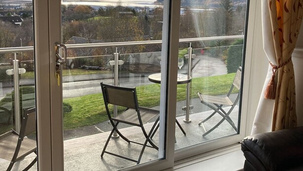 Een balkon met een glazen deur, een stoel en een tafel.
