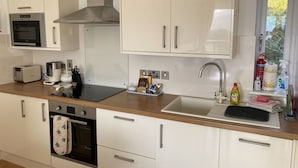 Een moderne keuken met witte kasten, een inbouwoven, een magnetron, een spoelbak en diverse keukenapparaten.
