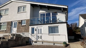 Een woonhuis met twee verdiepingen, een balkon, een trap en een kleine tuin.