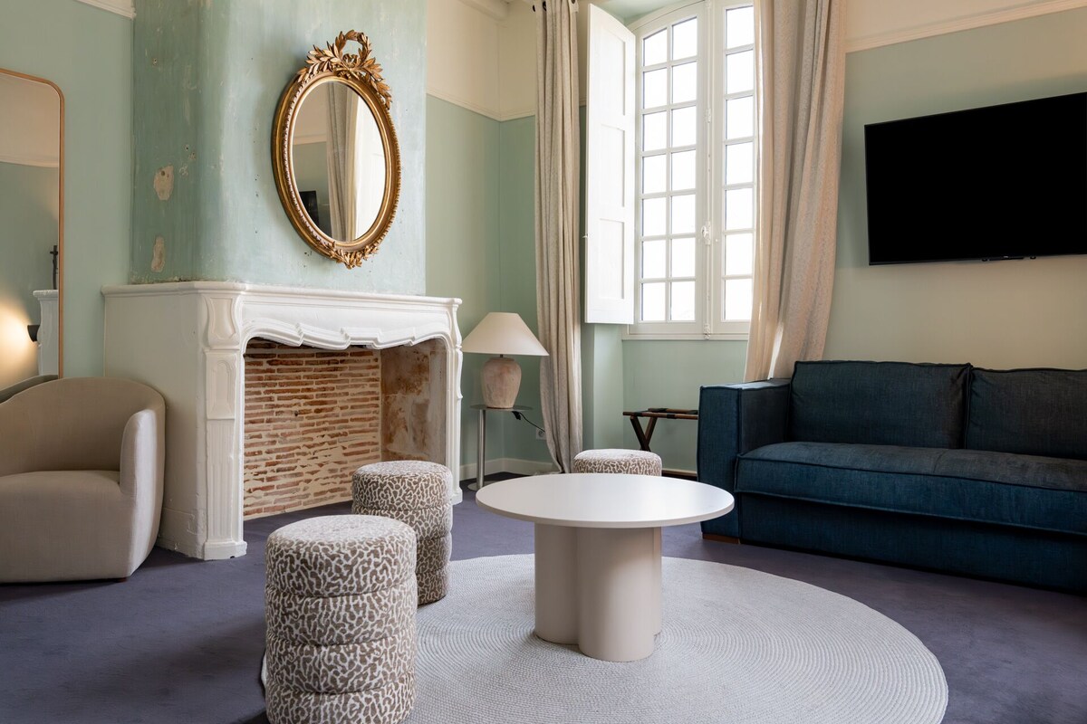 A living room with a fireplace, a round coffee table, ottomans, a sofa, and a TV mounted on the wall.