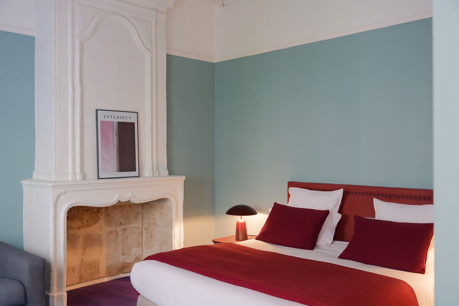 A bedroom with a bed, a fireplace, and a framed picture on the mantel.