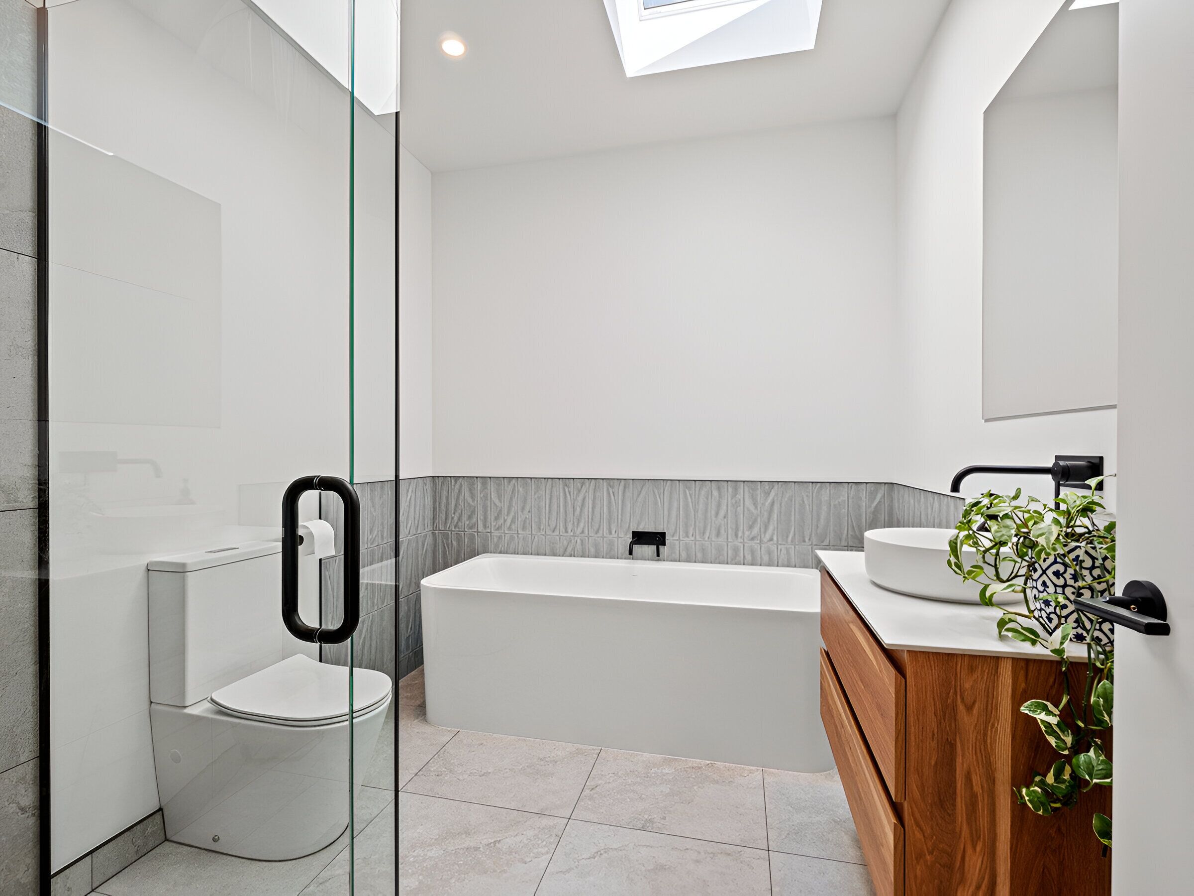 A modern bathroom with a glass shower enclosure, a toilet, a bathtub, and a vanity with a sink and mirror.