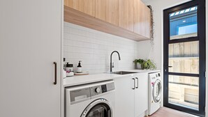 A modern laundry room with a washing machine, a sink, and wooden cabinets. - Cosy ski retreat on The Remarkables Ski Area. 5 minutes to Jacks Point Golf Club (Jacks Point)