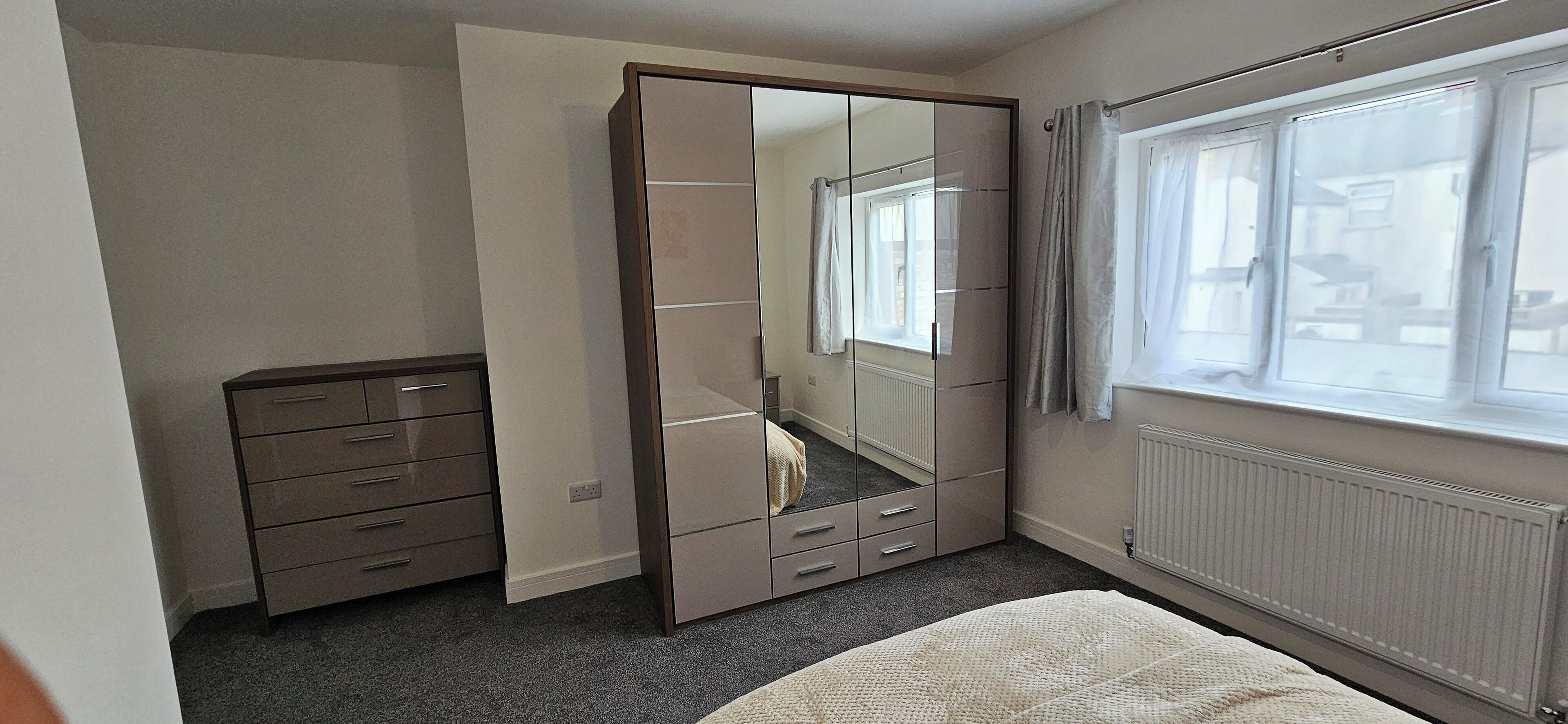 A bedroom with a bed, a dresser, a wardrobe with a mirror, and a window with curtains.