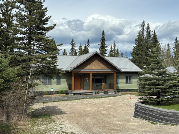 A lodge with a wooden front porch, a gravel driveway, and a surrounding forest. - Alpine Adventure at Jasper East Gates (Folding Mountain Village)