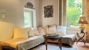 Una habitación acogedora con un sofá, una mesita y una lámpara. Se ve vegetación por la ventana.