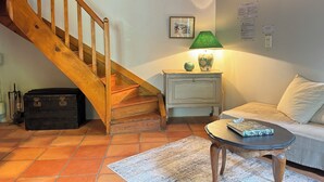Una sala de estar con una escalera de madera, una lámpara verde sobre una mesita de noche, un sofá y una alfombra estampada.