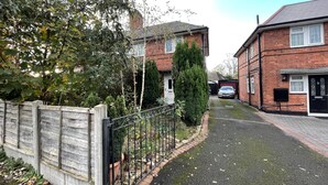 A residential street with houses, a car parked in the driveway, and a wooden fence. - Captivating 3-bed House in Nottingham (Nottingham)