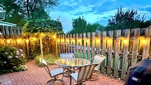A patio with a glass-top table and chairs, surrounded by a wooden fence with string lights. - The Perky Pineapple; Quiet Ranch; 2 King Beds; Well Appointed; Centrally Located (Raleigh)
