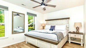 A bedroom with a large bed, two bedside tables, a ceiling fan, and a window with a view of greenery. - The Perky Pineapple; Quiet Ranch; 2 King Beds; Well Appointed; Centrally Located (Raleigh)