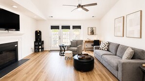 A living room with a fireplace, a ceiling fan, a sofa, a coffee table, and a TV. - The Perky Pineapple; Quiet Ranch; 2 King Beds; Well Appointed; Centrally Located (Raleigh)