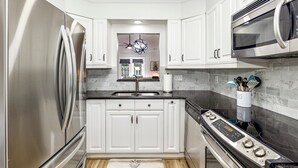 A modern kitchen with white cabinets, stainless steel appliances, and a marble backsplash. - The Perky Pineapple; Quiet Ranch; 2 King Beds; Well Appointed; Centrally Located (Raleigh)
