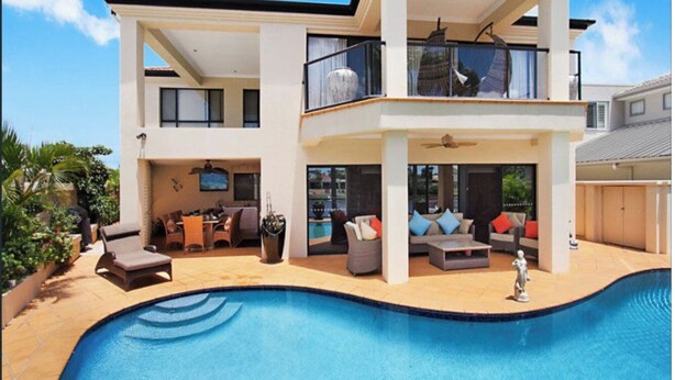 A modern two-story house with a swimming pool, outdoor seating, and a balcony. - Beautiful, Luxury, Water Front with Pool House (close to all amenities)  (Bundall)