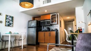 A compact kitchen with a refrigerator, microwave, and wooden cabinets. There is a dining table with chairs and a pendant light above it. - Amazing Studio Downtown MIA (Miami)