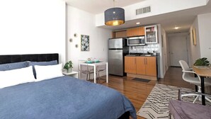 A modern bedroom with a large bed, a small table, and a kitchenette in the background. - Amazing Studio Downtown MIA (Miami)