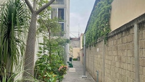 A narrow alleyway with a concrete path, flanked by a brick wall on one side and a building with a glass facade on the other.