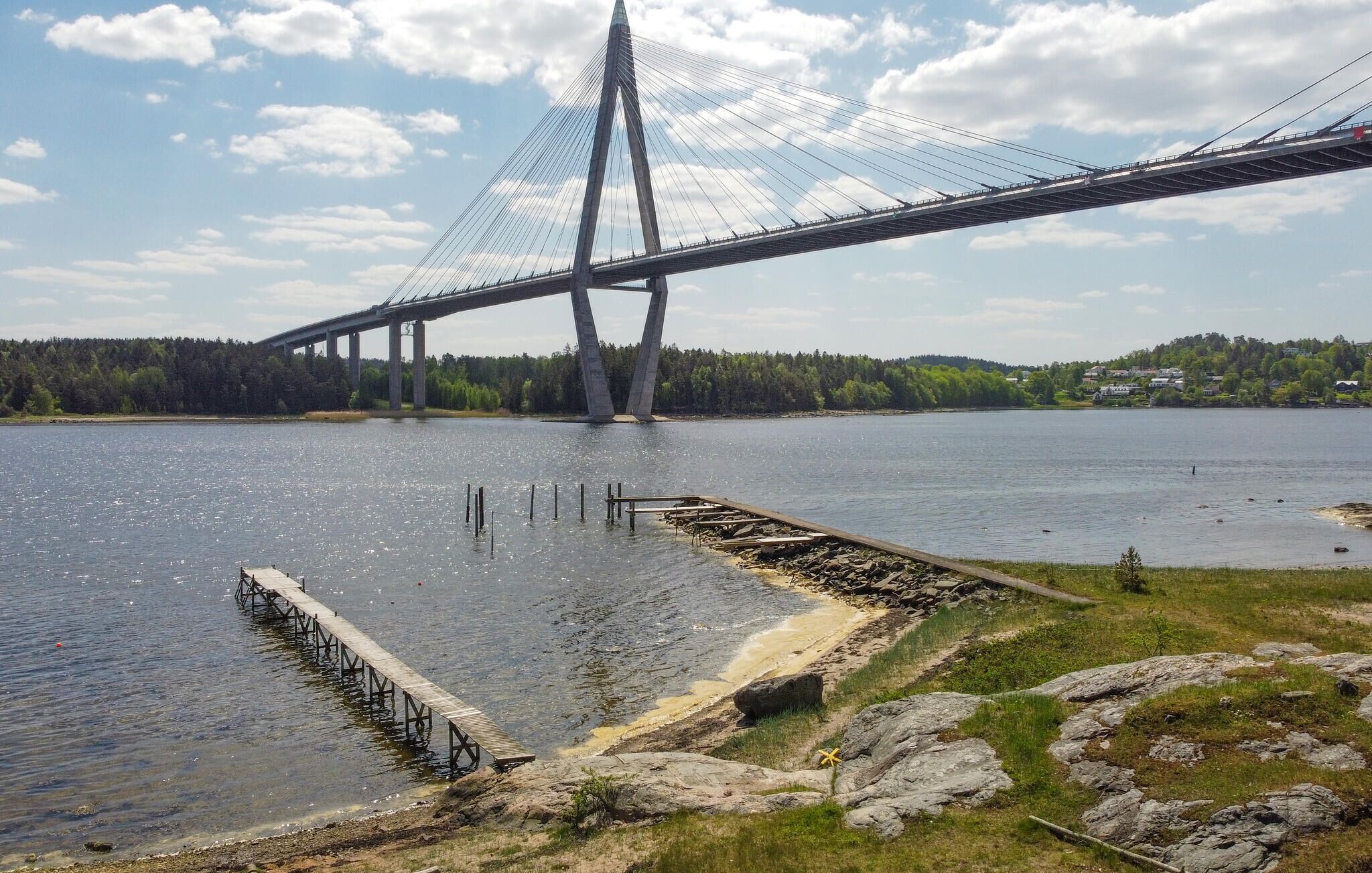 Un grand pont suspendu enjambe un lac paisible, et une jetée en bois s’avance dans l’eau.