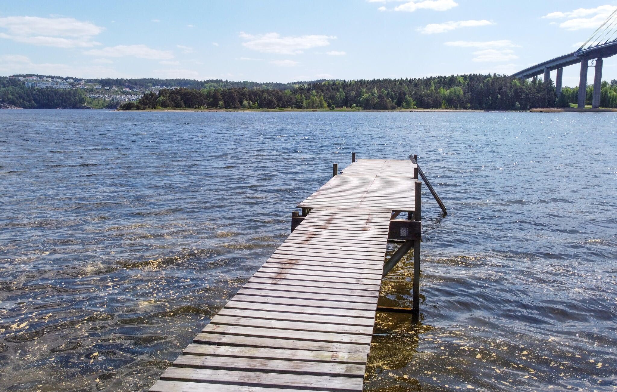 Un muelle de madera que se adentra en una masa de agua, con un puente al fondo.