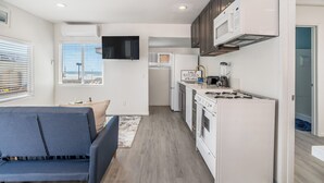 A compact kitchen with white appliances, a flat-screen TV, and a view of the ocean through the window.