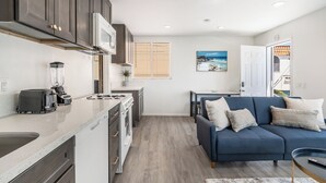 A compact kitchen with a microwave, toaster, and blender, a blue sofa with cushions, and a dining area with a table and chairs.