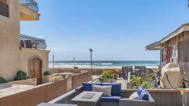 A rooftop patio with outdoor seating, a view of the ocean, and a wooden building with a balcony.