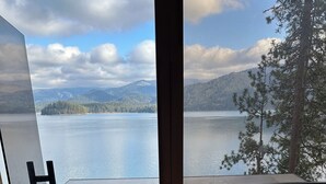 A view from a balcony with a wooden railing, overlooking a calm lake and distant mountains.