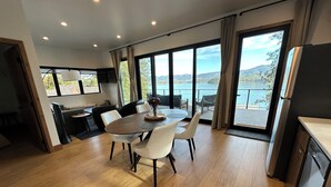 A modern kitchen with a large island, dining area with a round table and chairs, and large windows offering a view of a lake and mountains.
