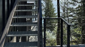 A metal staircase leading to a building with a view of tall trees and a body of water.