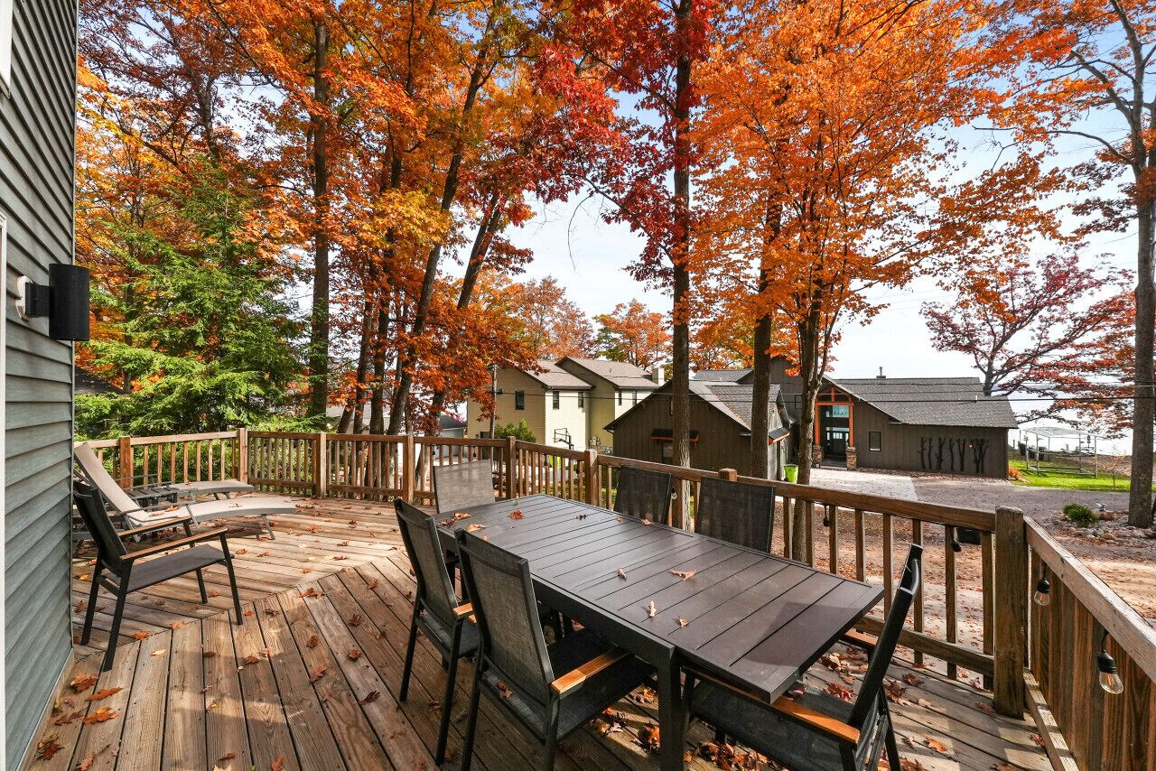Un patio in legno con tavolo e sedie, circondato da alberi dai colori autunnali.