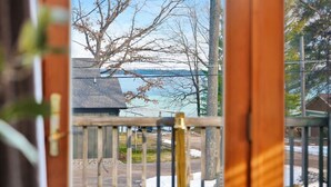 A view through a wooden door with a metal gate, leading to a backyard with a tree and a house in the background. - Lake View Fully Stocked Family Retreat - Paddleboards, Firepit, Games, EV outlet (Roscommon)