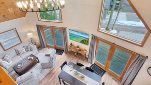 A spacious living area with a high ceiling, large windows, a dining table, and a cozy seating arrangement. - Lake View Fully Stocked Family Retreat - Paddleboards, Firepit, Games, EV outlet (Roscommon)