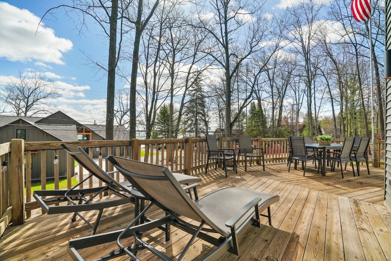 A wooden deck with lounge chairs and a table, surrounded by trees and a view of houses.