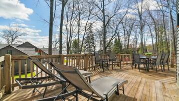 A wooden deck with lounge chairs and a table, surrounded by trees and a view of houses.