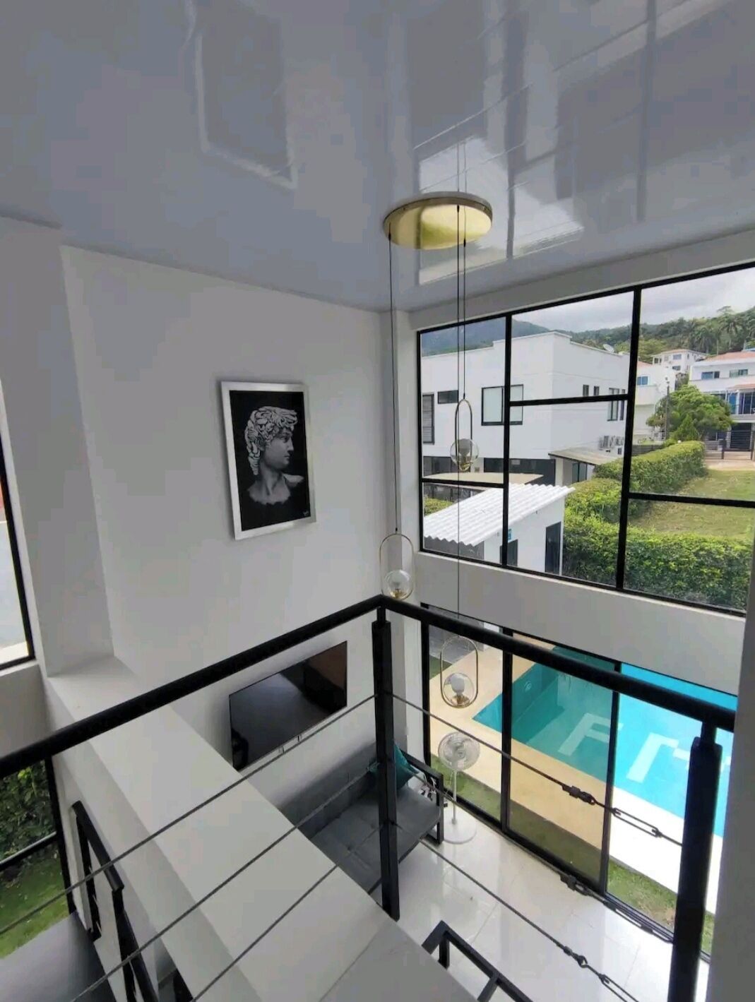 Un interior moderno con una escalera de cristal, una obra de arte enmarcada y vistas a una piscina y edificios al exterior.