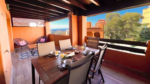 A dining area with a wooden table set for two, chairs, and a view of the cityscape.