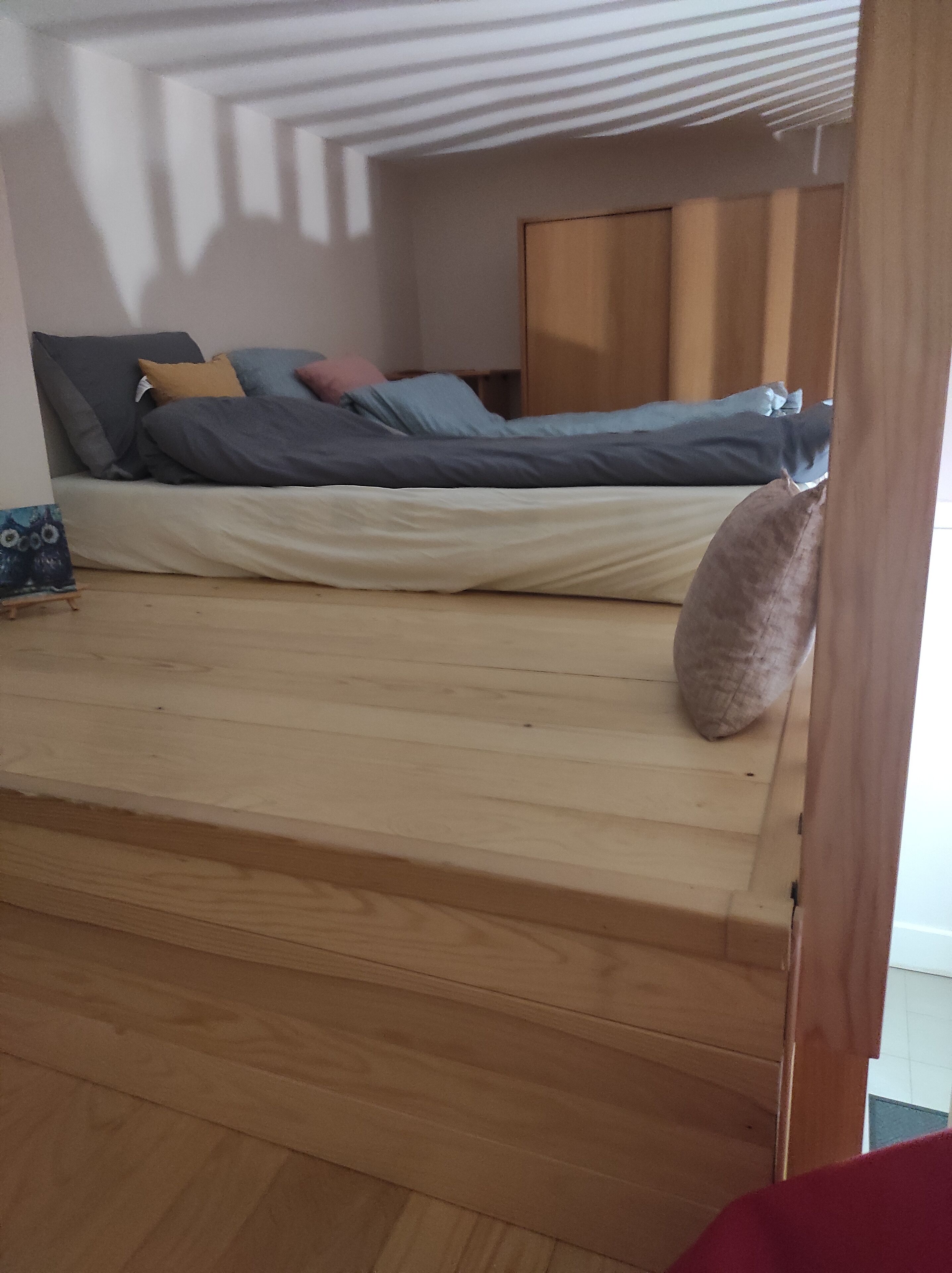 Une petite chambre avec un lit simple, un plancher en bois et un plafond en pente.