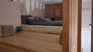 A bedroom with a bed, pillows, and a wooden floor.