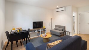 Un salon moderne comprenant un canapé, une table basse, un téléviseur et un coin repas avec des chaises et une table préparée pour le petit-déjeuner.