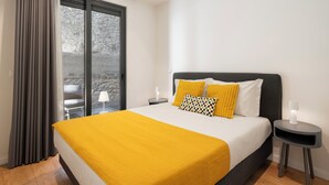 Une chambre moderne avec un grand lit, une vue à travers une porte vitrée et une petite table avec une lampe.
