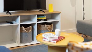 Un salon moderne avec un téléviseur à écran plat, une lampe jaune, une bibliothèque et une table basse sur laquelle sont posés des livres et une tasse.