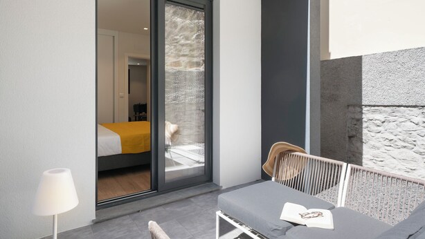 Une chambre moderne dotée d’une porte-fenêtre coulissante donnant sur un balcon, d’un lit recouvert d’une courtepointe jaune et d’un coin salon avec une table et des chaises.
