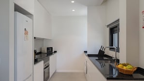 A modern kitchen with white cabinets, a black countertop, a microwave, a sink, and a basket of fruit. - Holidays in Funchal - Golden City B (Funchal)